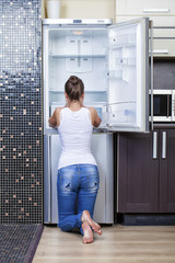 Fototapeta na wymiar Unhappy and hungry girl near empty fridge