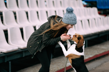 Fototapeta na wymiar Young hipster girl with her pet estonian hound dog playing, junping and hugging and having fun outdoor at the old stadium.