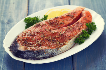 fresh salmon with herbs and lemon on white dish on blue wooden background