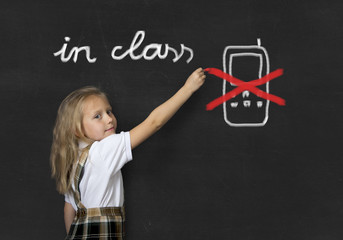 young sweet junior schoolgirl writing with chalk about not using mobile phone in school class