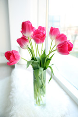 Beautiful fresh tulips in glass vase on windowsill, indoors