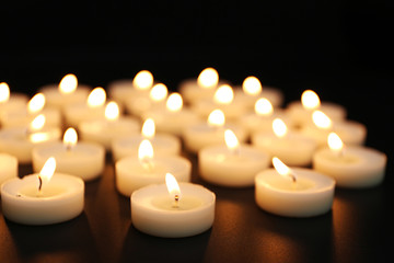 Alight candles in a row on black background, blurred