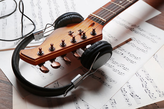 Electric guitar and headphones with music notes on wooden background, close-up