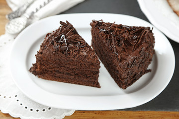 Sliced chocolate cake on wooden table, on light background