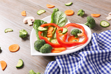 Useful cut vegetables on a plate in the form of heart on wooden table top view