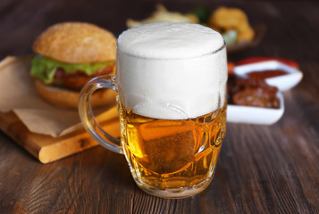 Glass mug of light beer with snacks on dark wooden table, close up