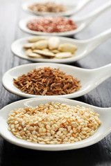 Different kinds of seeds in spoons on wooden table