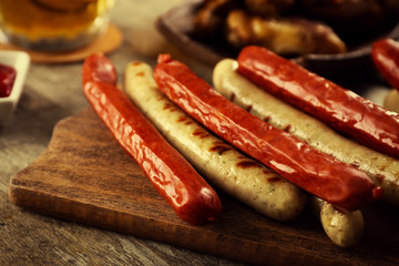 Glass of beer, chicken wings and grilled sausages on wooden table, close up