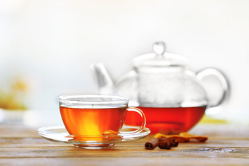 Glass cup of tea with teapot on wooden table against blurred background