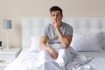 Sleepy young man rubbing his eye in bed at home