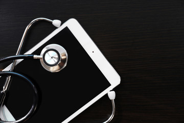 Fototapeta na wymiar Stethoscope and tablet on dark wooden background