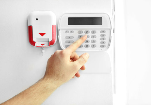 Male hand entering code on security system keypad indoors