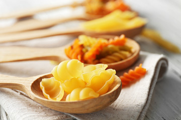 Different types of pasta in spoons on wooden table closeup