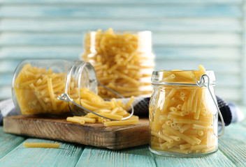 Raw pasta in glass jars on wooden background