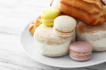 Plate of cakes and macaroons on wooden background, closeup