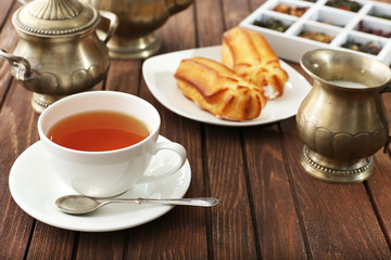 Cup of tea and pastry filled with custard on wooden background