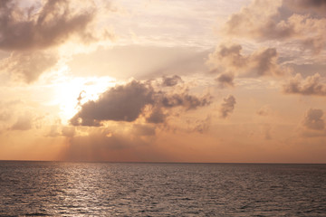 Fototapeta premium Golden sunset over calm ocean water with dramatic clouds and sun rays breaking through sky, the horizon line separates the tranquil sea from the colorful evening sky