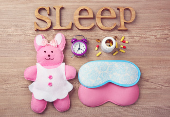 Word Sleep with pills, little toy and sleeping masks on a wooden background