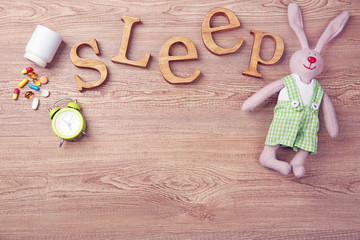 Word Sleep with pills and little toy  on a wooden background