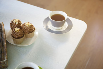 Cup of tea and creamy chocolate cupcakes on wooden table indoors