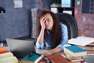 Tired girl with pile of books in office