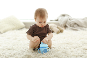 Baby with a drinking bowl sitting on carpet