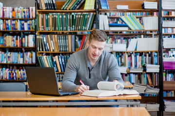 Male student with laptop studying in the university library