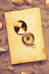 Fototapeta na wymiar Vintage book and compass on sandy beach