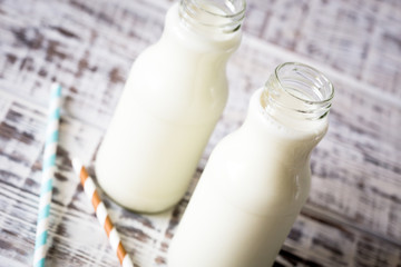 Two bottles of milk with striped straws standing on old table.