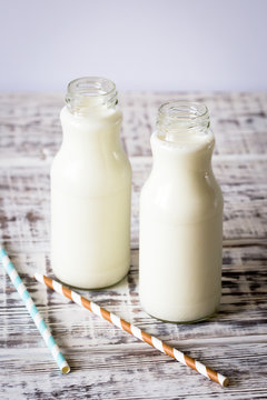Two bottles of milk with striped straws standing on old table.