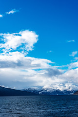 view over fjord in Norway, with mountains in the background under a blue sky with white clouds