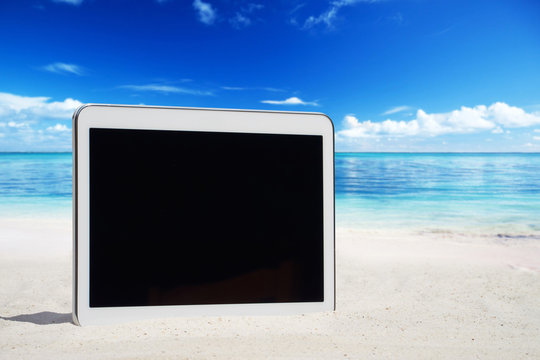 Weisses Tablet mit leerem Touchscreen Display steck im Sand mit einem Seestern am Meeresstrand