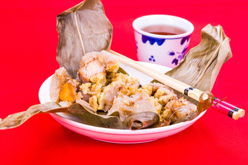 Steamed Chinese rice dumpling or zongzi served with oriental tea on red background