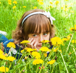 Portrait of sad little girl with big eyes in the meadow with dandelions