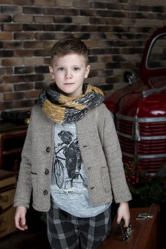 Beautiful boy in a jacket and a scarf on a background of red retro car. Retro style