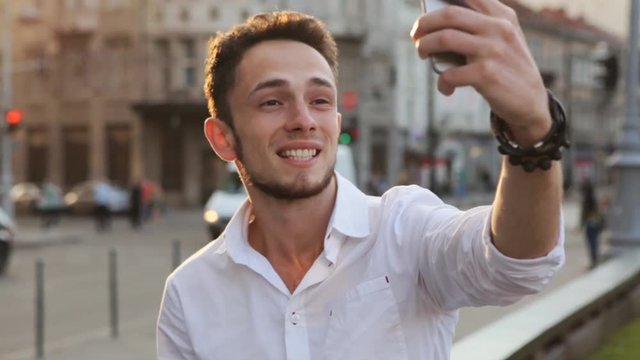 Young man taking panorama picture by using his smartphone. Handsome caucasian male in his 20s doing selfie outdoors. Guy using frontal camera on his device.
