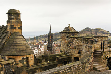 View over Edinburgh Castle's wall towards Old Town and the slopes of Arthur's Seat and Holyrood Park, with church towers and historic buildings