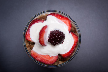Traditional English dessert strawberry trifle with blackberries in a transparent glass on a plate of slate. Flat lay