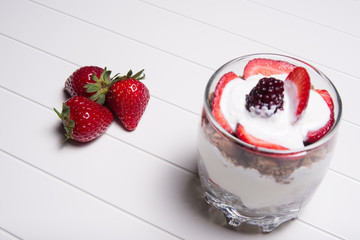 Traditional English dessert strawberry trifle with blackberries in a transparent glass on a white background with strawberries