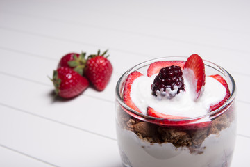 Traditional English dessert strawberry trifle with blackberries in a transparent glass on a white background with strawberries