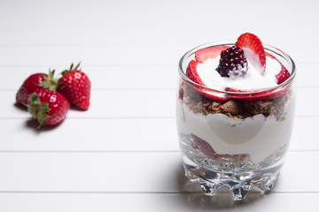 Traditional English dessert strawberry trifle with blackberries in a transparent glass on a white background with strawberries