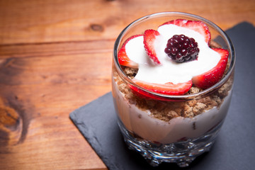 Traditional English dessert strawberry trifle with blackberries in a transparent glass on a rustic wooden surface on a plate of slate. Free space for text