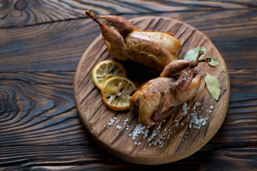 Rustic wooden serving board with baked quails, studio shot