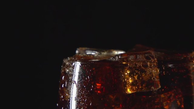 SLOW: A cola drink in glass with ice on a black background