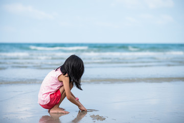 child girl sitting and playing on white sand beach