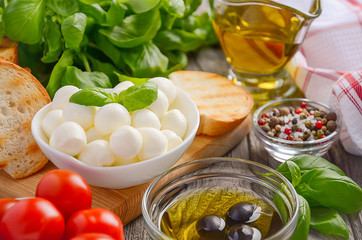 Italian food ingredients – mozzarella, tomatoes, basil and olive oil on rustic wooden background, selective focus