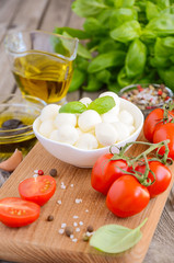 Italian food ingredients – mozzarella, tomatoes, basil and olive oil on rustic wooden background, selective focus