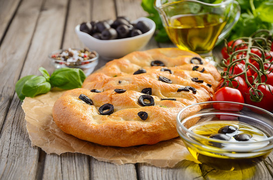 Italian focaccia bread with olives and rosemary on rustic wooden background, selective focus, copy space