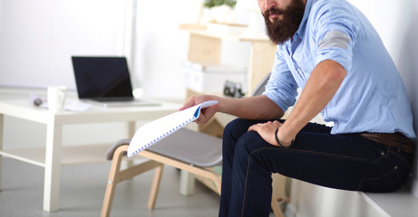 Young businessman sitting on chair with book in office