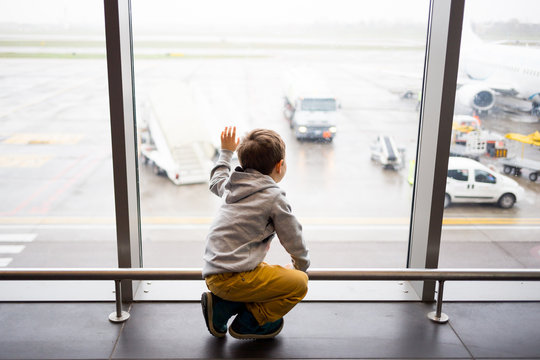 kid waiting in the airport terminal looking out the window to the planes